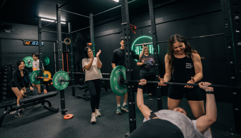 Gym coaches and members cheering on a member doing bench presses
