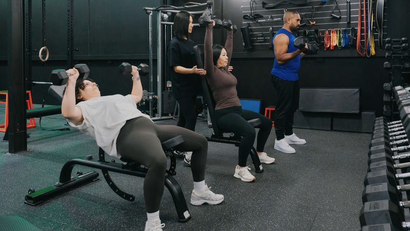 A personal trainer coaching a client through a strength training exercise inside a modern gym.