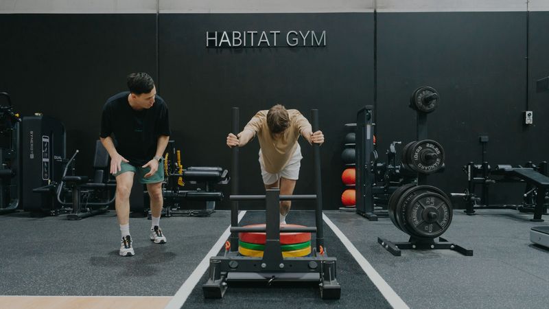 A personal trainer coaching a client through a strength exercise in a modern gym while closely monitoring their form.