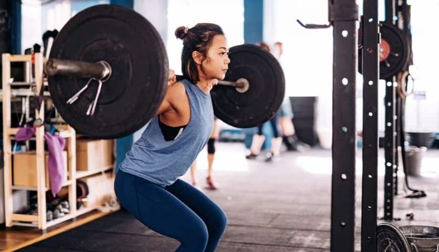 Asian woman performing a barbell squat at the gym, focusing on strength and form.