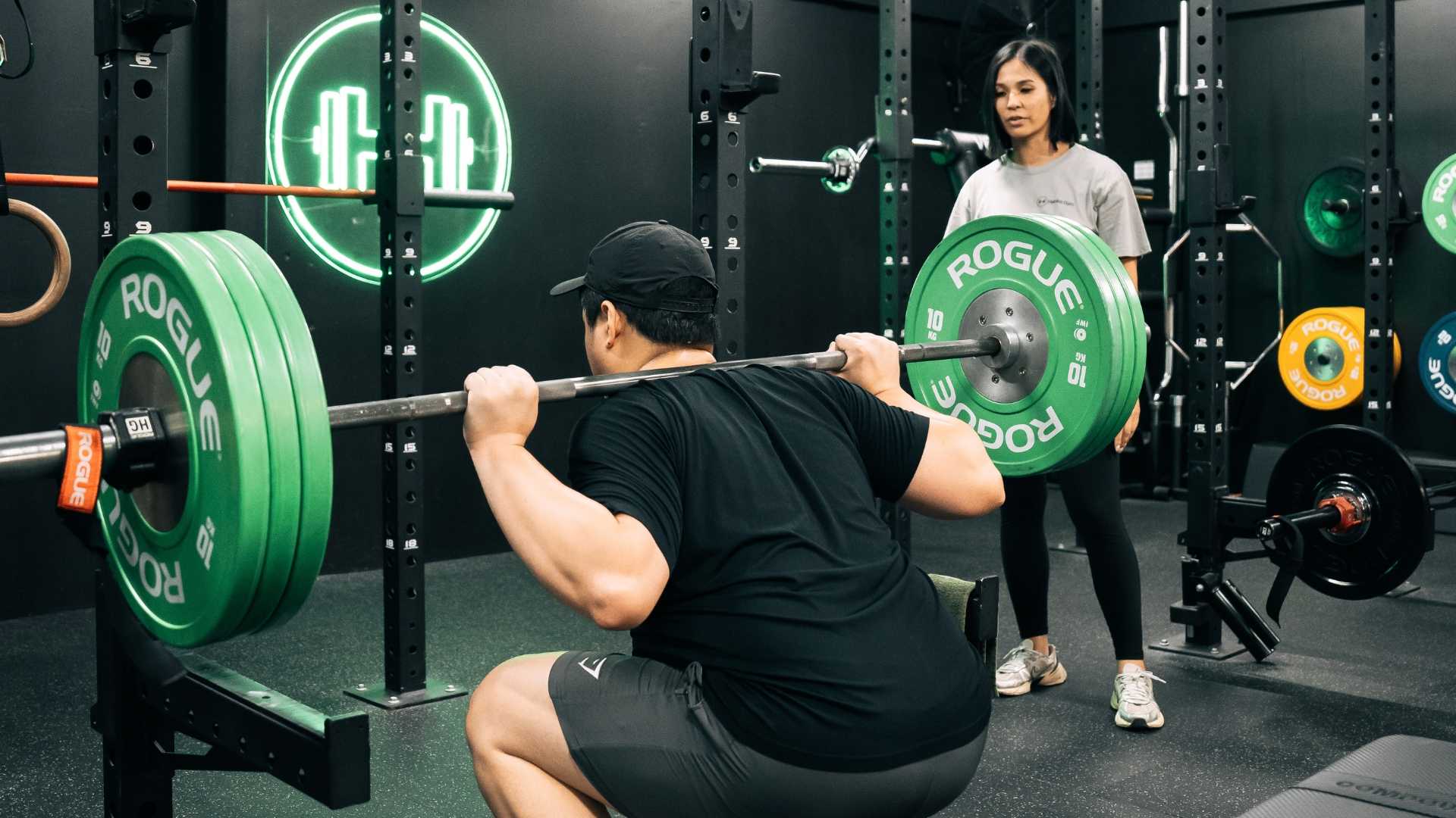 Client doing a barbell squat with coach's guidance at Habitat Gym