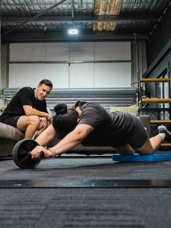 Personal trainer, Coach Ben spotting client during ab roller exercise inside Habitat Gym in Western Sydney