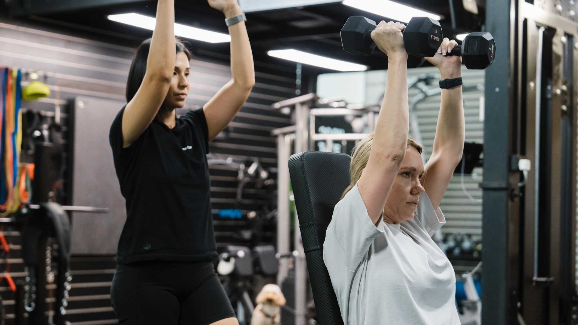 Personal trainer guiding a client in the gym, demonstrating proper form.