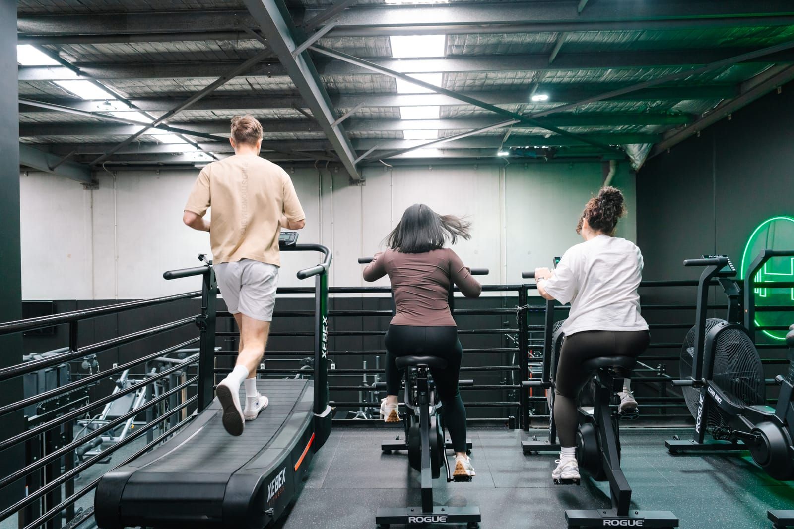 Members working side by side on a curved treadmill and Rogue Echo bikes on the cardio mezzanine
