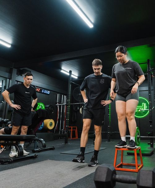 Trainer observing female member’s fitness form in Habitat Gym's strength zone