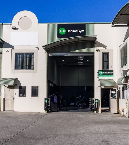 Habitat Gym’s Prestons shopfront on a clear day, roller door open with equipment racks visible beneath the green entry signs
