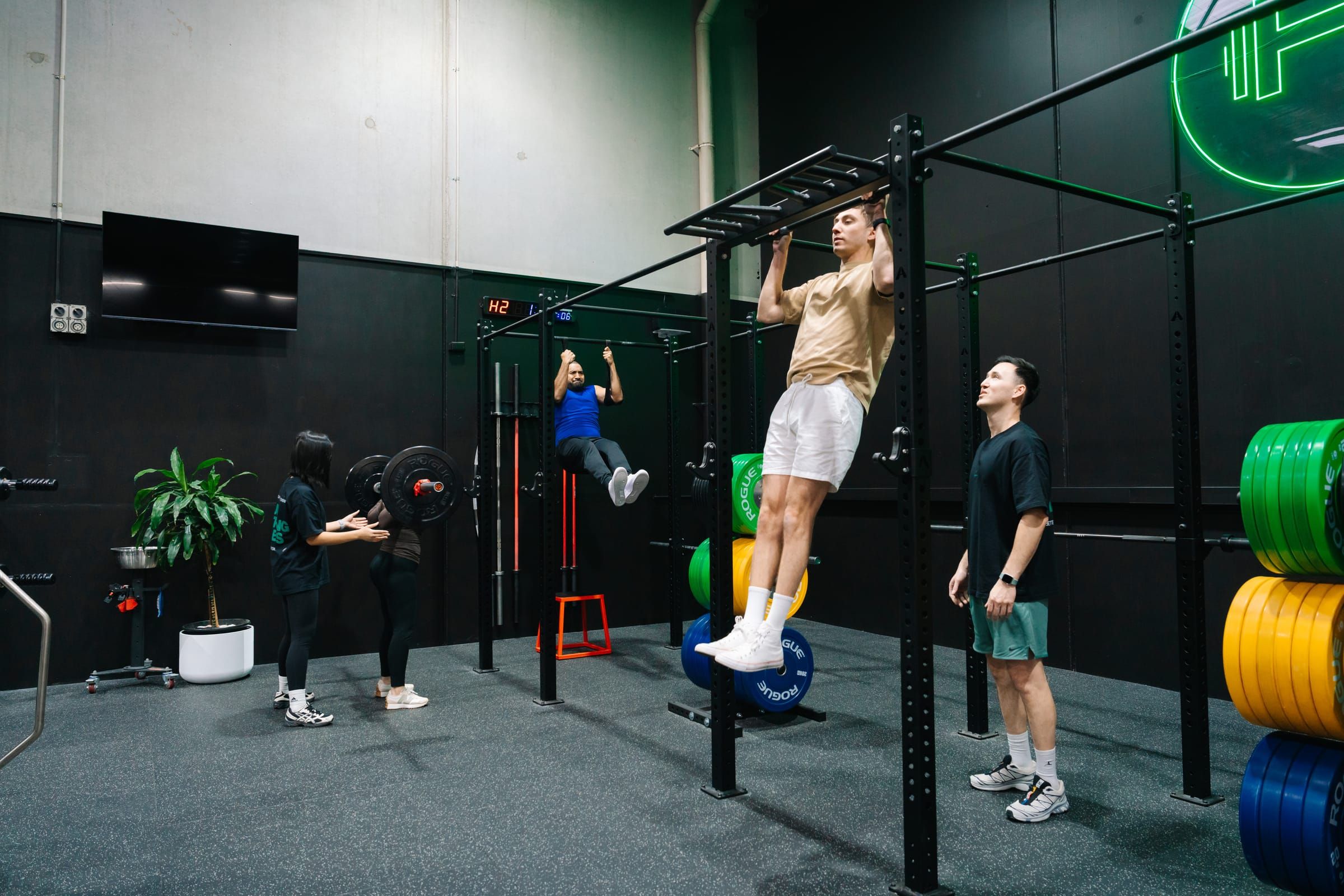 Members practising pull-ups on the rig while a coach works with others nearby at Habitat Gym in Prestons