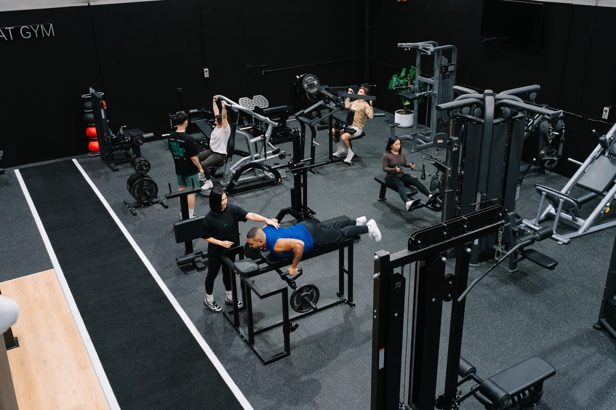 View across the floor of Habitat’s private gym in Prestons as members train on benches and machines, a coach adjusting one client’s rowing position