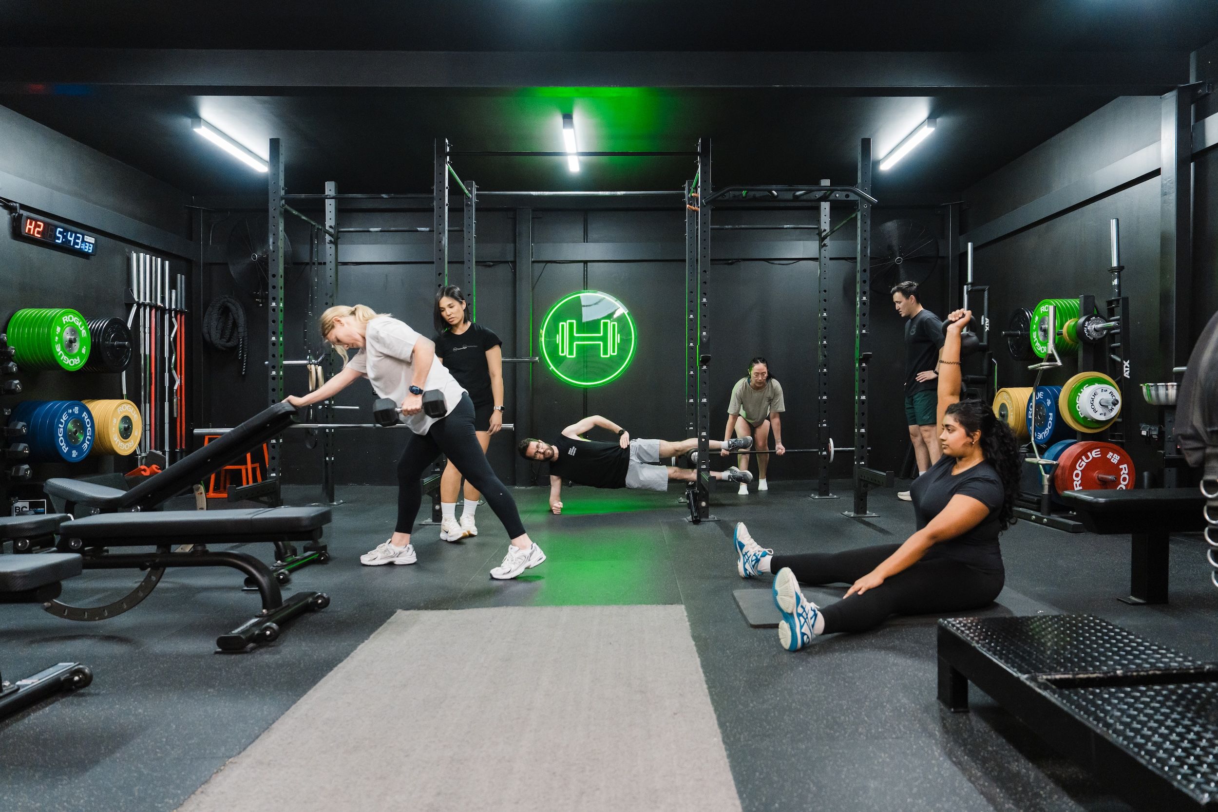 Multiple clients training together with dumbbell rows, stretching, and strength exercises at Habitat's private gym in Prestons