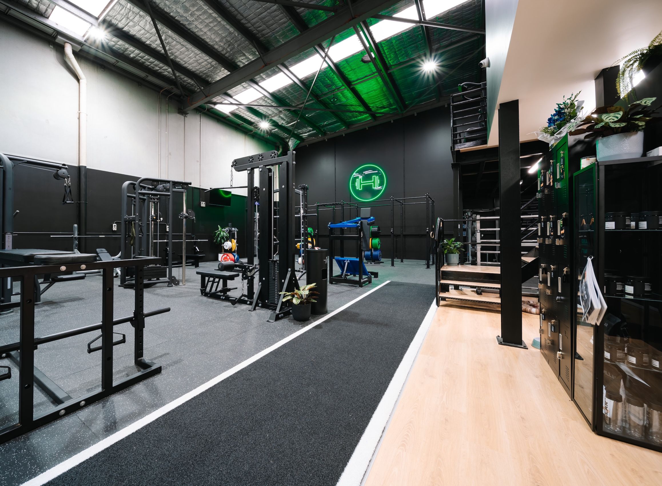 Functional trainers, benches and a sled track inside Habitat’s private gym, the green neon dumbbell sign glowing on the back wall