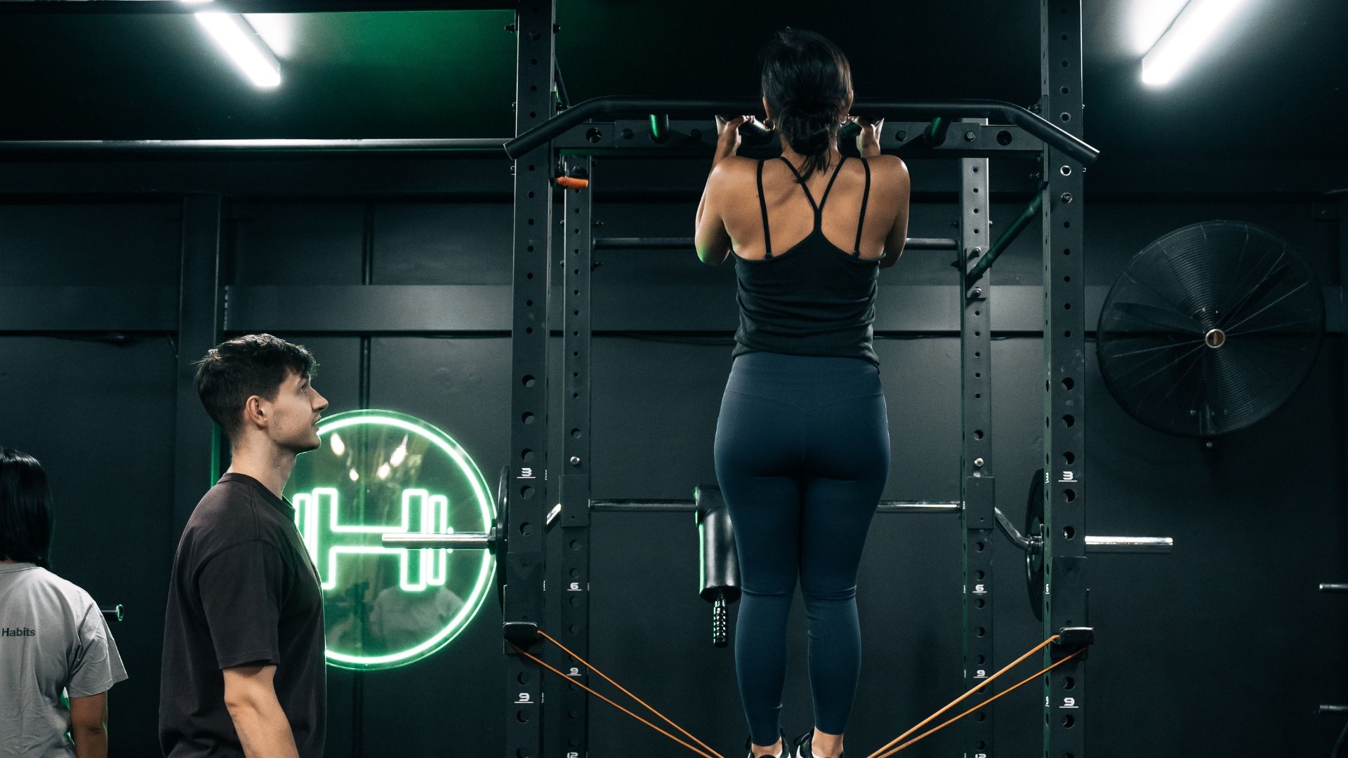 Personal trainer coaching a client through assisted pull-ups during a strength training session, focusing on proper form and control.