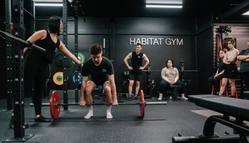Coach Jeannie correcting gym member's technique whilst lifting weights inside their private gym