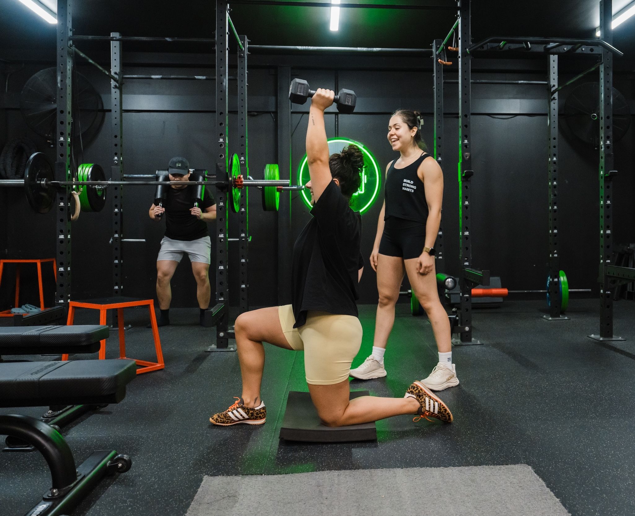 Client performing a kneeling dumbbell press while a personal trainer coaches beside her at Habitat's private gym in Prestons, Sydney