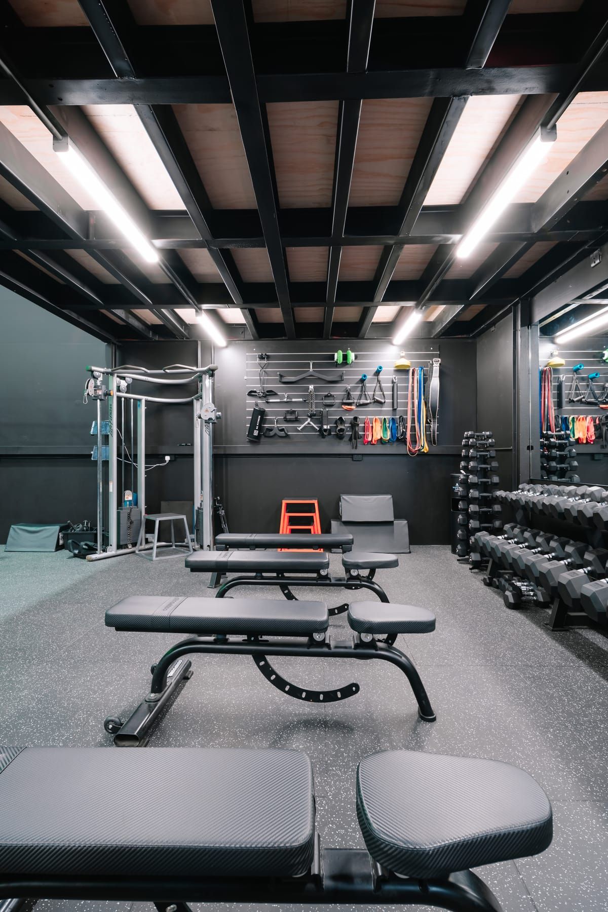 Private training room with adjustable benches, racked dumbbells and a cable machine under a timber-lined ceiling