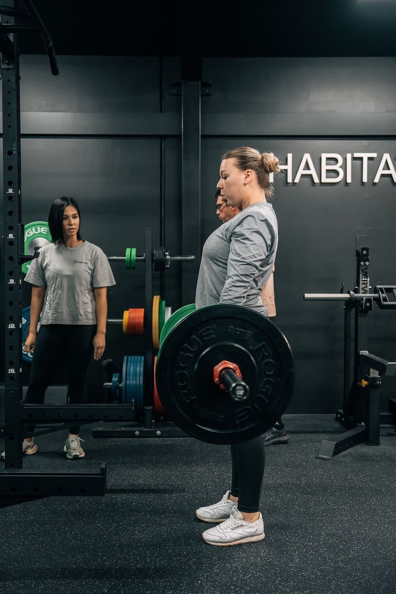Personal training session at Habitat Gym – a female coach observing a client performing a barbell deadlift in a small group strength training environment