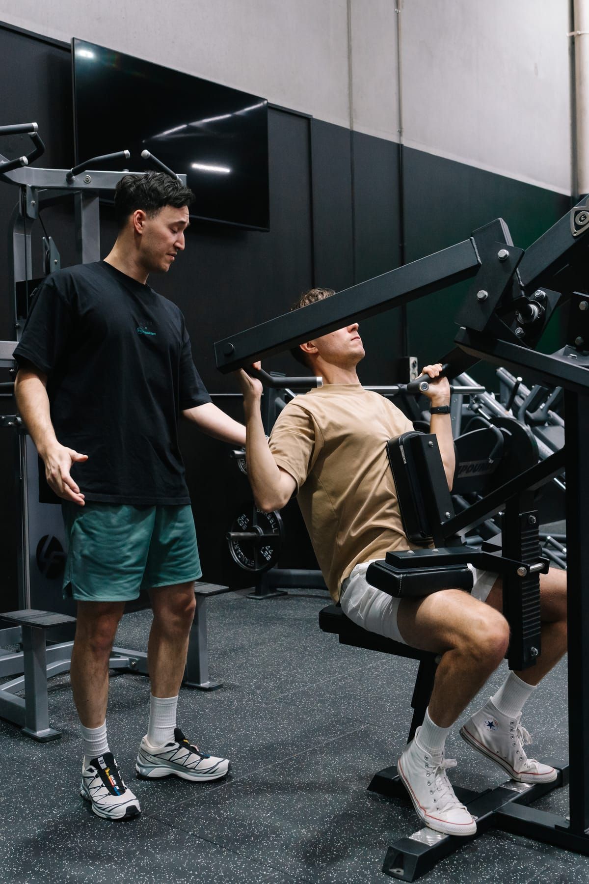 Coach guiding a member through a set on a plate-loaded press machine at Habitat Gym