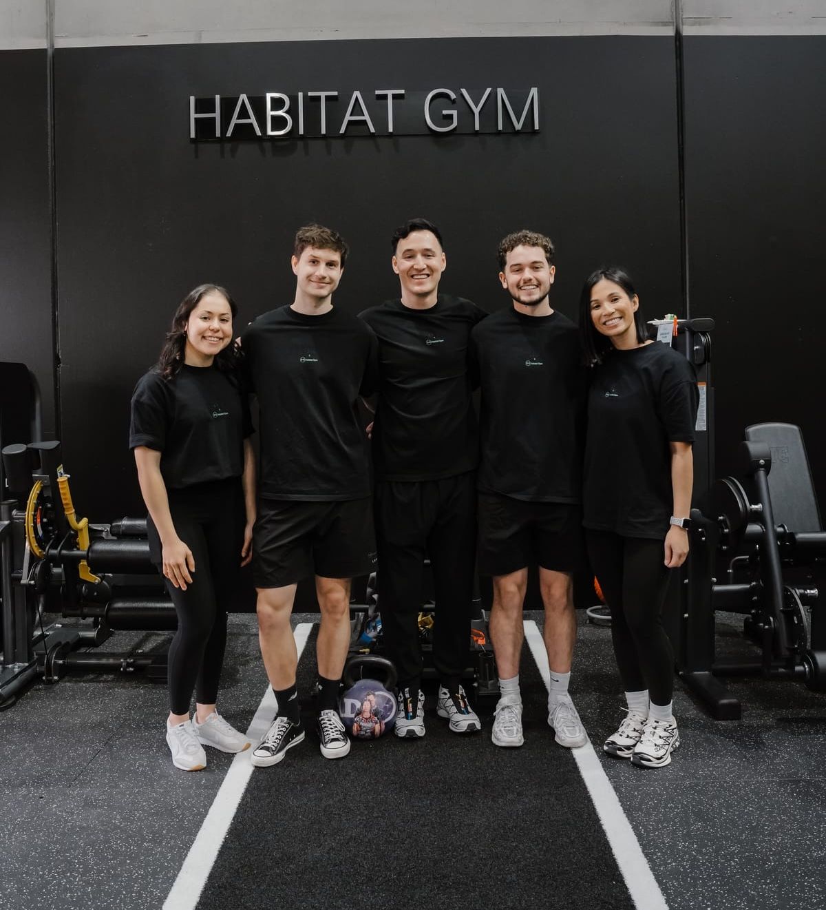 Habitat Gym’s coaching team standing arm in arm beneath the Habitat Gym sign