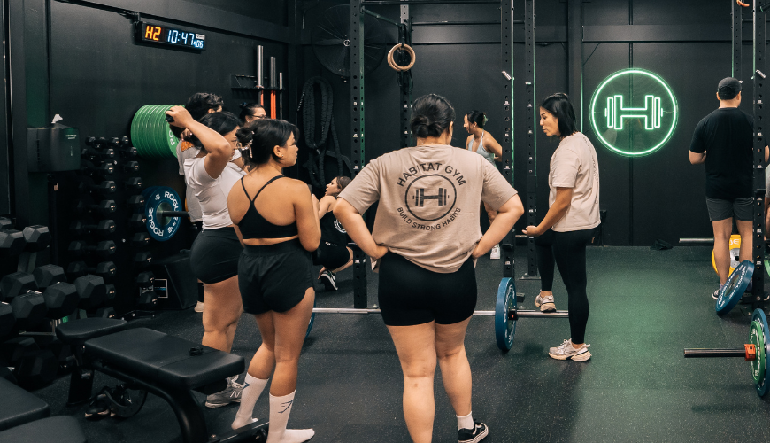 Women gathering around in an indoor group fitness setting inside Habitat Gym with functional equipment