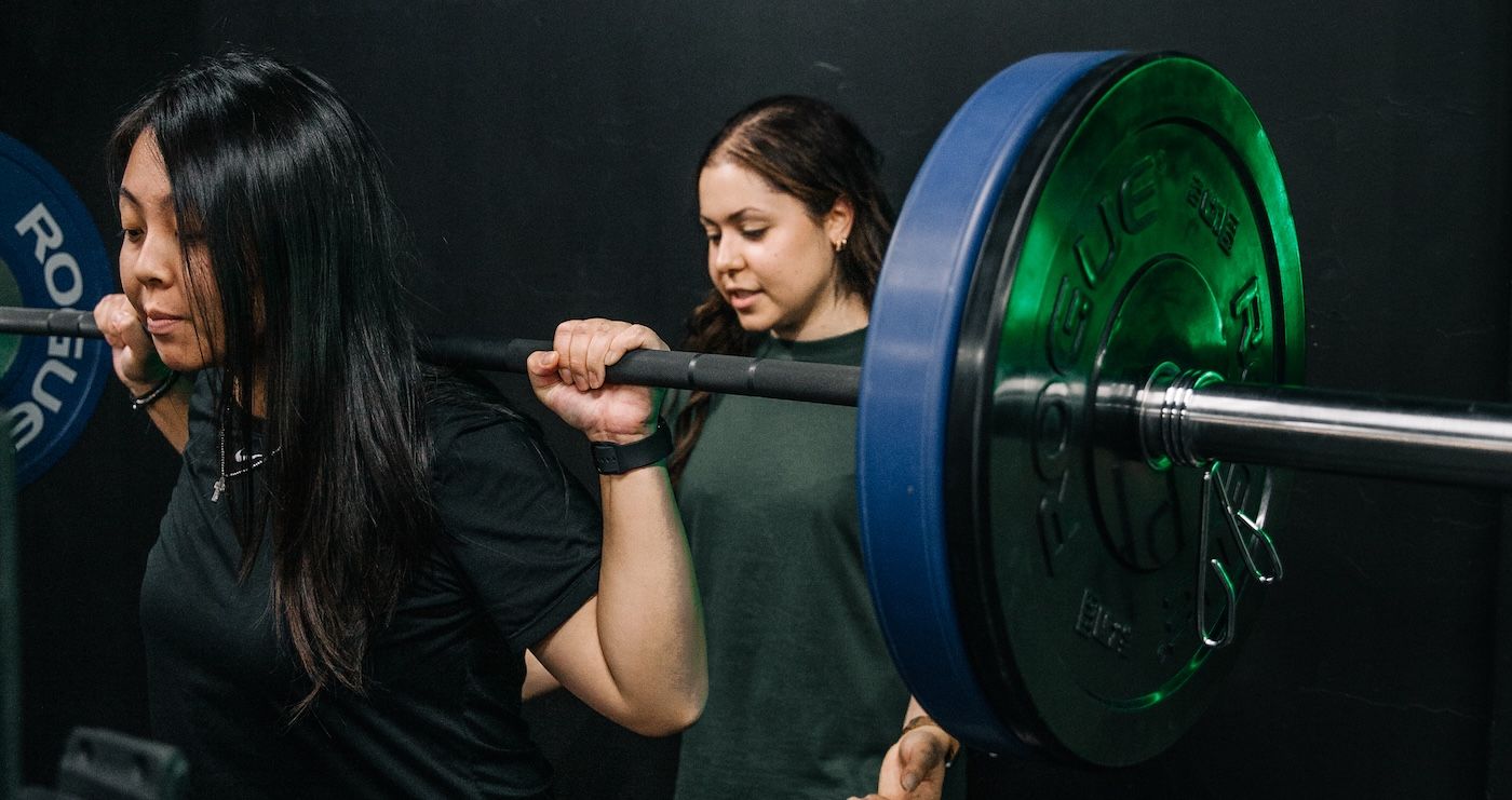 Woman being guided by her trainer in barbell squat training at Habitat Gym