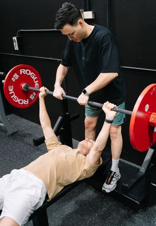 Coach spotting a member bench pressing a barbell loaded with red Rogue bumper plates