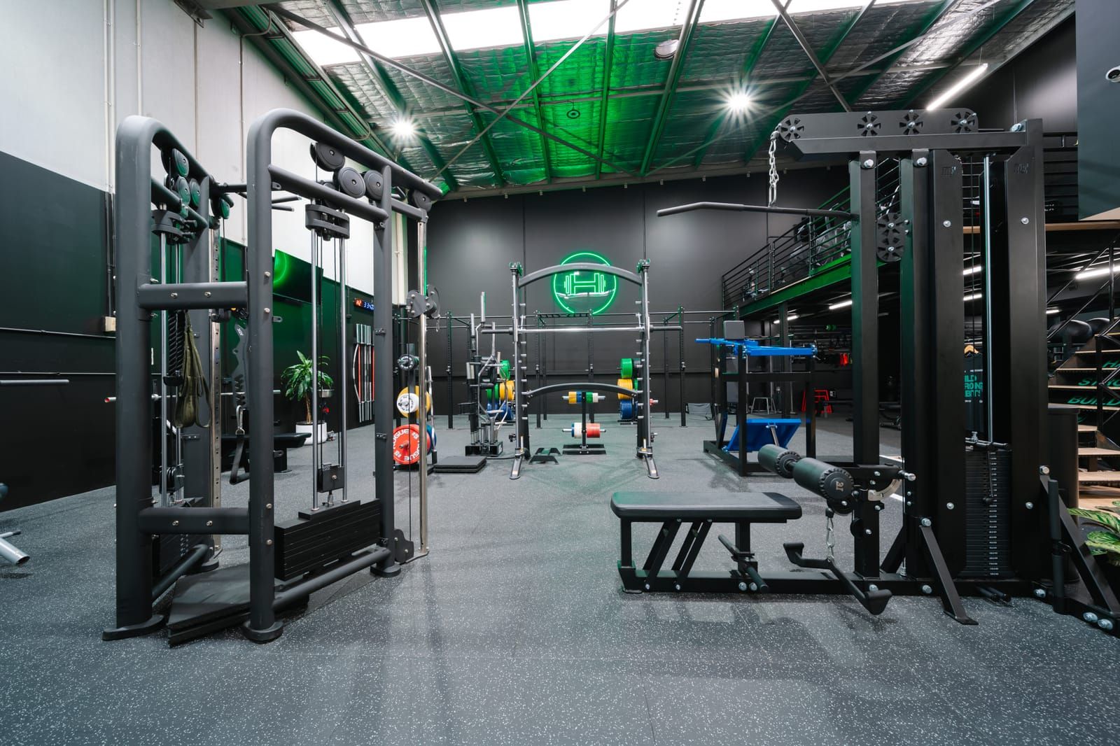 Cable stations framing a power rack and barbells under the green-lit ceiling of the strength zone