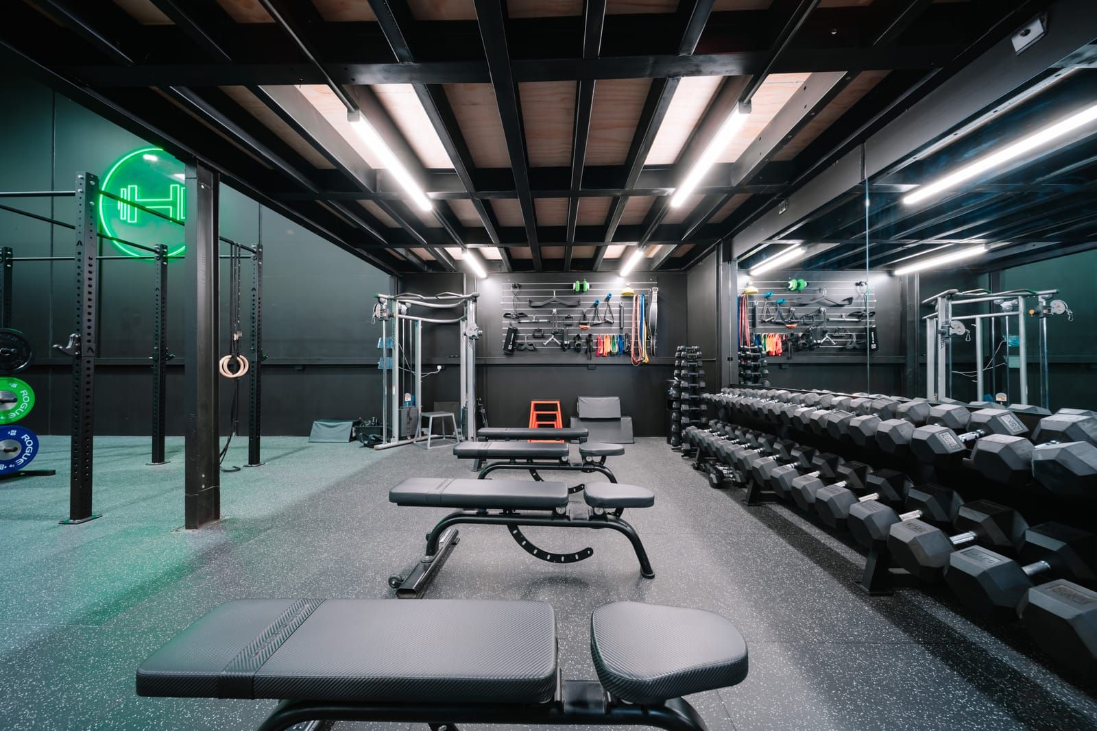 Dumbbell room at Habitat Gym in Prestons with adjustable benches, mirrored dumbbell racks and a glowing neon sign