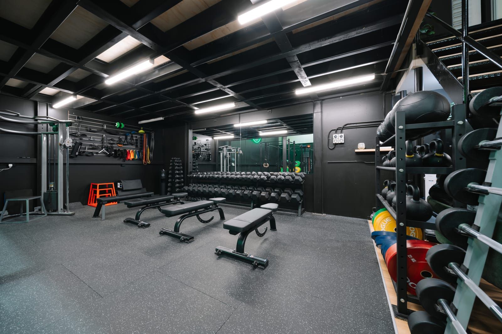 Flat benches lined up in the dumbbell room, with slam balls and bars stored along the wall