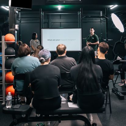 Members seated at a Habitat Gym workshop reflecting on their biggest insights, with coaches presenting at the front of the room
