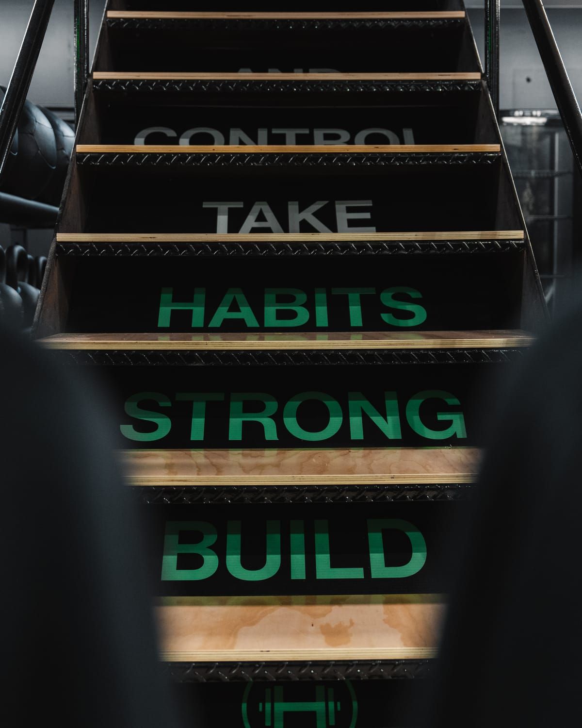 Green ‘Build strong habits, take control’ lettering climbing the stair risers at Habitat Gym