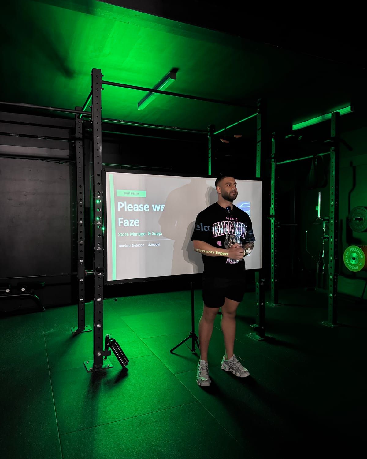 Coach presenting beside a projector screen inside the green-lit rig at Habitat Gym