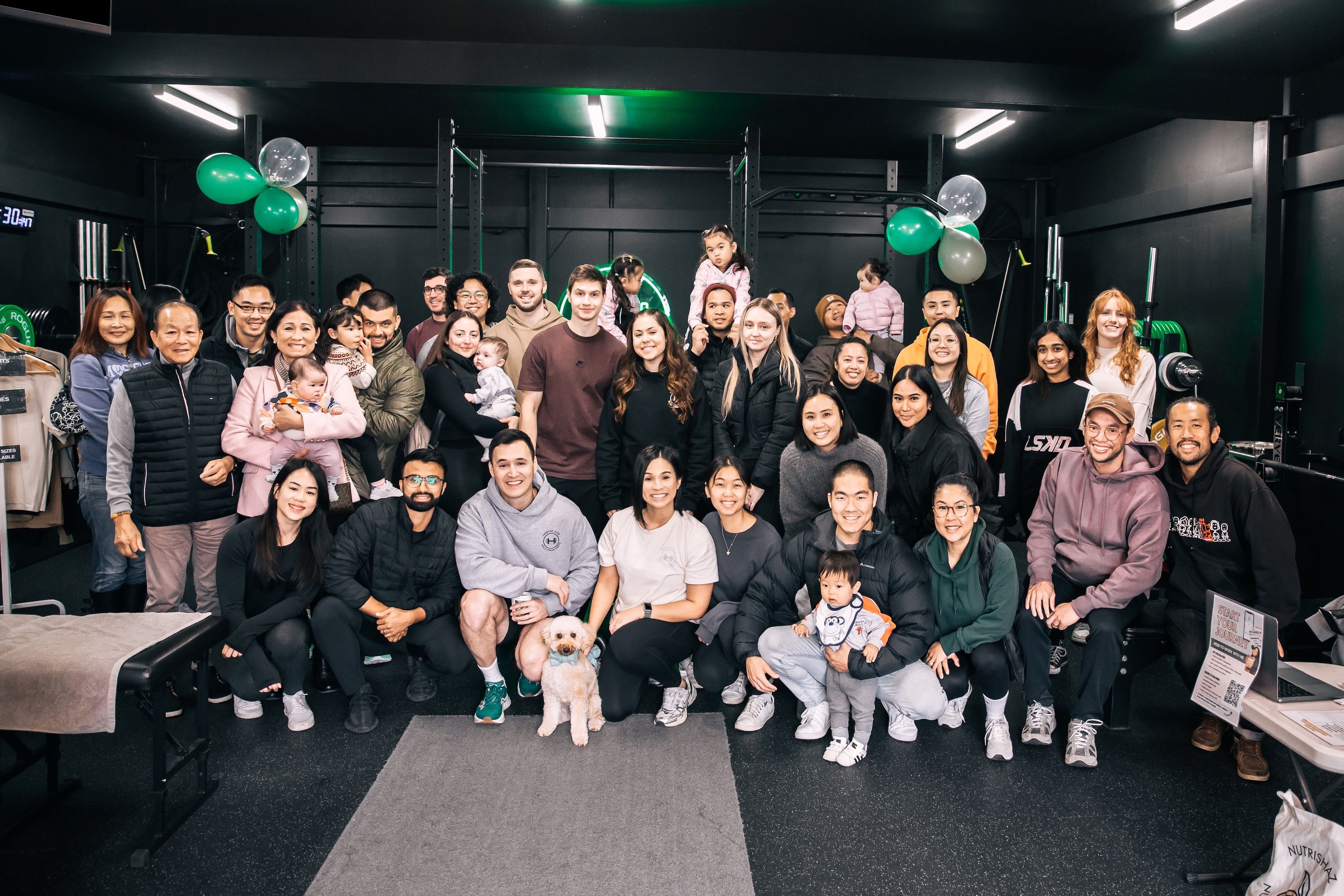 Members, families, and staff celebrate the opening of Habitat Gym, gathered together inside the facility decorated with green and white balloons